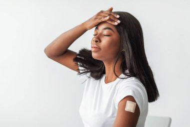 COVID-19 aşısının yan etkileri. Coronavirus antiviral enjeksiyonundan sonra koluna dokunan alnına pansuman yapılan hasta, baş ağrısı, yüksek vücut ısısı...