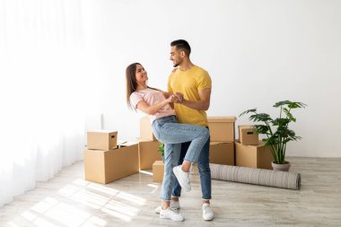 Bir çift, taşınan kutular ve bitkilerle dolu boş bir dairede neşeli bir dansın tadını çıkarıyor. Gülümsemeleri yeni evlerini kutlarken mutluluğu gösteriyor..