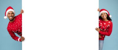 Renkli bir Noel süveteri ve Noel Baba şapkası giymiş mutlu bir çift açık mavi bir arkaplanda duruyor, ellerinde kocaman boş bir tabela, yüzlerinde gülücükler, bayram kutlamalarına hazırlar..