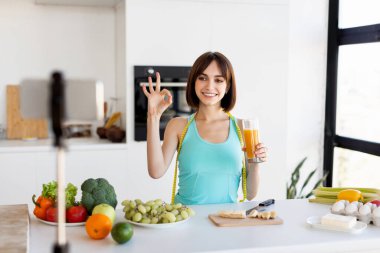 Genç bayan parlak mutfağında bir bardak taze meyve suyu tutarak ve 