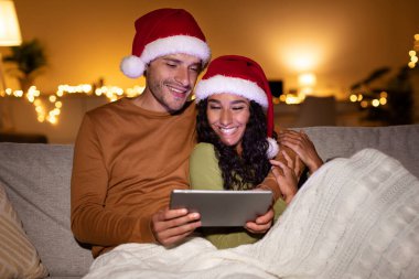 Kanepeye kıvrılıp yatmış kırmızı Noel Baba şapkaları takmış ve tabletten Noel filmleri seyrediyor. Sıcak ortam neşeli bir bayram kutlaması için mükemmel..