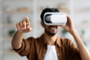 Genç bir adam evde rahat bir ortamda sanal gerçeklik deneyiminden zevk alır. Bir VR kulaklık takıyor ve elini uzatıyor. Çevresindeki dijital dünyayla iç içe..