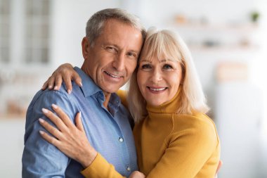 İçerde rahat bir ortamda kucaklaşırken neşeli bir çift birbirine sıcak bir şekilde gülümsüyor. Yumuşak gün ışığı sevinçlerini ve yakınlıklarını vurgular.