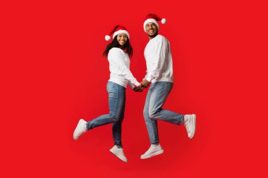 Neşeli bir çift el ele tutuşup mutlu mesut zıplıyor. Aynı Noel şapkalarını takıyorlar. Onların neşeli ifadeleri tatil sezonunun neşeli ruhunu yansıtır..