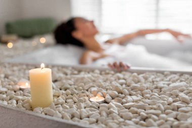 Bir insan, beyaz taşlar ve yumuşak mum ışığıyla çevrili rahatlatıcı bir spa anından zevk alır. Atmosfer huzurlu, rahatlamak ve kendine bakmak için mükemmel..