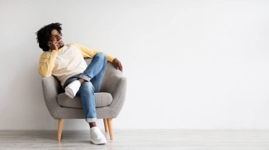 Neşeli genç bir adam gri bir koltukta rahatça oturur ve hoş bir telefon görüşmesi yapar. Rahat ve mutlu görünüyor, sıradan giyinmiş. Aydınlık ve davetkar bir ortam..