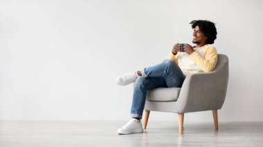 Genç ve mutlu bir Afro-Amerikalı adam bir sandalyede rahatlar ve kahvesini yudumlar. Yan tarafa bakarken gülümsüyor, evdeki basit bir ortamda sakin bir anın tadını çıkarıyor..