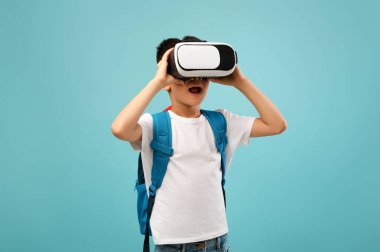 Bir çocuk, sanal gerçeklik kulaklığı kullanırken tamamen meşgul olan yumuşak mavi bir arka plana karşı duruyor. Dijital bir dünyayı keşfederken gözleri şaşkınlık içinde genişliyor..