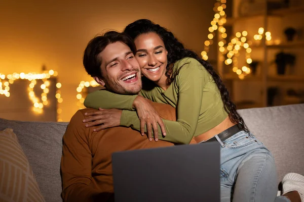 Sevimli çift, rahat oturma odalarında dizüstü bilgisayarlarıyla internette gezinirken kucaklaşıyorlar. Birlikte vakit geçirmeyi seviyorlar, akşamlarını evde geçiriyorlar..