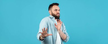 Sakallı ve günlük kıyafetleri olan bir adam sağlam bir mavi arka plana karşı durmaktadır. Ellerini kaldırır, sanki dur ya da hayır der gibi, kişisel alana olan ihtiyacını açıkça ifade eder..