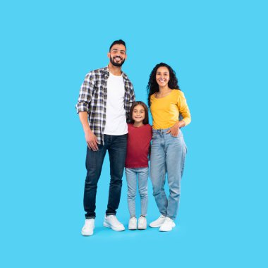 Neşeli bir aile, parlak mavi bir geçmişi olan renkli bir stüdyoda bir arada duruyor. Baba, anne ve kız, günlük kıyafetlerini giyerken gülücüklerini paylaşıyorlar..