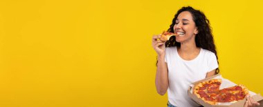 Kıvırcık saçlı bir kadın pizza kutusunu tutarken bir parça pizza yer. Mutlulukla gülümsüyor, yemekten zevk aldığını gösteriyor. Parlak sarı arka plan canlı atmosfere ekleniyor..
