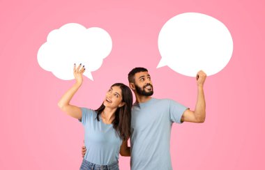 Bir çift şakacı bir şekilde sohbet ediyor, konuşma baloncukları tutuyor. Gülümsüyorlar ve sevinçlerini ifade ediyorlar. Neşeli pembe arka plan, etkileşimlerinin canlı atmosferini arttırır..