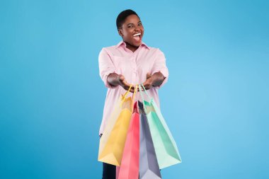 Neşeli bir kadın elinde parlak renkli alışveriş torbalarıyla davetkar bir gülümsemeyle ayakta duruyor. Alışveriş macerası için heyecanlı görünüyor..