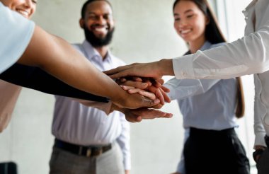 Parlak bir ofis alanında, çeşitli genç profesyonellerden oluşan bir grup sevinçle ellerini birleştiriyor. Gülümserler, başarılı bir projeden sonra takım çalışmasını ve işbirliğini kutlarlar..