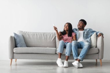 Sistemi böl. Tatmin olmuş Afro-Amerikan kadın elinde uzaktan kumandayla klima altında rahatlıyor, milenyum siyahi çifti oturma odasında kanepede oturuyor, bedava fotokopi alanı.