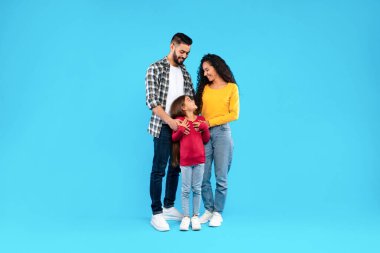 Mutlu bir aile neşeli bir atmosferle bir arada durur. Anne ve baba, neşeli anlarını güzelleştiren günlük giysiler giyerek karşılık veren kızlarına bakarlar..