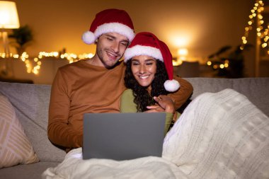 Sıcak bir battaniyeye sarılı, Noel Baba şapkası takmış bir çift kanepeye oturur. Mutlu bir şekilde dizüstü bilgisayarda Noel filmleri izliyorlar. Etrafları hafif ışıklandırma ve neşeli bir atmosferle çevrili..