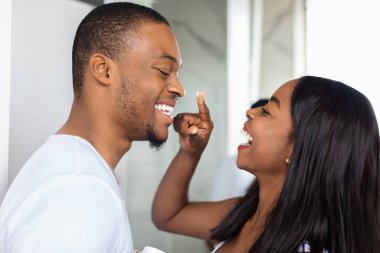 Genç bir çift evlerinde neşeli ve neşeli bir anı paylaşıyor, yüzlerine gülücükler ve pasta kreması bulaşmış. Güneş sıcak bir atmosfer yaratır..