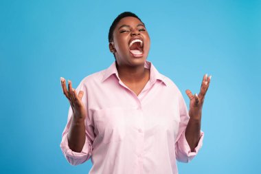 Bir kadın duygularını tutkulu bir şekilde elleri havada ifade eder. Kısa saçları var ve açık pembe bir gömlek giyiyor, koyu mavi bir arka fona karşı..