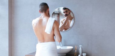 Çağdaş bir tuvalette duran bir adam kendini yuvarlak bir aynanın önünde hazırlıyor. Üstsüz, beline bir havlu takmış, tımar etmeye odaklanmış. Boşluk temiz bir tasarım içeriyor.