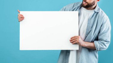 Bir adam elinde parlak mavi bir arka plana karşı beyaz bir tabela tutarken gülümsüyor. Ayar parlak ve iyi aydınlatılmış, yaratıcılık ve duyurular için uygun görünüyor..