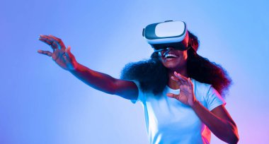 Genç bir kadın sanal gerçeklik deneyimi yaşıyor, kulaklık takıyor ve uzanırken gülümsüyor. Titreşimli ışık, onun heyecanını arttıran canlı bir atmosfer yaratıyor..