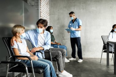 Babası klinikte COVID-19 'a karşı aşı bekleyen genç oğlunu, Kafkas ailesini, aşı merkezini ziyaret eden hastaları, koronavirüs konseptine karşı aşı bekleyen