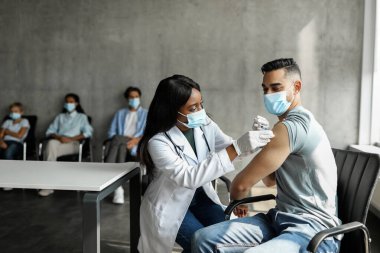 Arap hasta COVID-19 'a karşı kaslar arası iğne oluyor, siyah kadın doktor genç adama omuz yapıyor, koruyucu maskeler takıyor, uzay kopyası yapıyor.