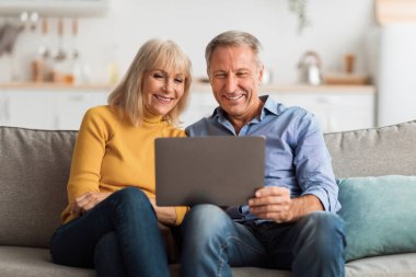Bir çift kanepede oturuyor, tabletten bir şey izlerken gülümsüyor. Parlak ve misafirperver oturma odalarında rahat ve mutlu görünüyorlar..