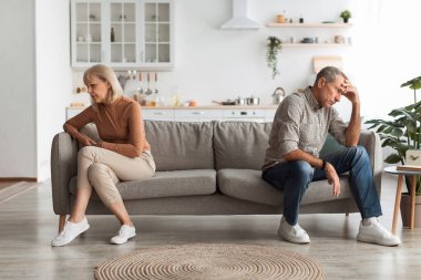 Modern bir oturma odasındaki bir kanepede oturan bir çift duygusal sıkıntı belirtileri gösteriyor. Kadın, erkek sıkıntılı görünürken yüzünü çevirir ve ciddi bir atmosfer yaratır..