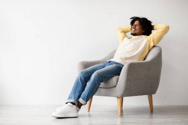 Mutlu bir siyah adam evinde rahat bir koltukta dinlenerek vakit geçirmekten zevk alır. Gözleri kapalı, elleri başının arkasında, huzurlu ve rahatlatıcı bir ortamda gülümsüyor..