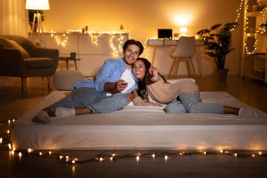 Bir çift bir yatakta dinleniyor, birlikte film izliyorlar. Evlerinde rahat ve sıcak bir atmosferle çevrili uzaktan kumandayı tutarken kamerayı gösteriyorlar..