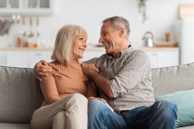 Mutlu, yaşlı bir çift kanepede birlikte otururken sıcak ve sevgi dolu bir etkileşimi paylaşıyor. Neşeli atmosfer aralarındaki güçlü bağı ve bağı yansıtıyor..