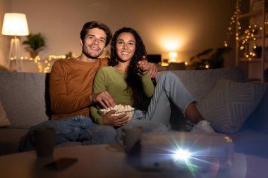 Bir çift rahat oturma odalarındaki kanepede rahatlar, projektör kullanarak birlikte film izlerler. Patlamış mısır yer ve birbirlerini kucaklarlar, hafta sonlarını evde geçirirler..