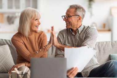 Neşeli bir çift, parlak oturma odalarındaki bir kanepede oturur, gülümser ve keyifli bir anı paylaşırlar. Önemli belgeleri tartışırken şakacı bir şekilde etkileşime geçiyorlar..