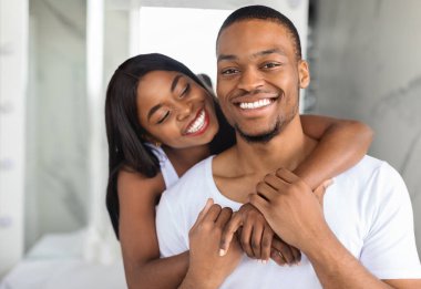 Mutlu bir çift birbirlerini kucaklıyor, sıcak bir gülümsemeyle, parlak ve neşeli bir atmosferle. Güneş ışığı kapalı alandaki neşeli ifadelerini aydınlatır..