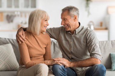İki yetişkin evdeki kanepede birlikte keyifli bir anın tadını çıkarıyor. Gülümserler ve sohbet ederler. Oturma odalarında sıcak ve sevgi dolu bir atmosfer yaratırlar..