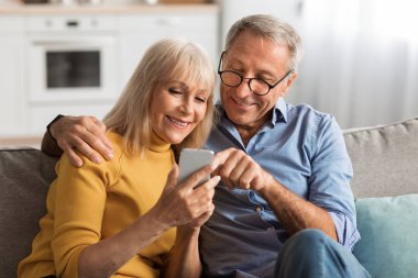 Mutlu bir çift oturma odalarındaki bir kanepede oturup birlikte akıllı telefona bakıp gülümseyip gülerken bir anlarını paylaşıyorlar. Hava sıcak ve davetkar..