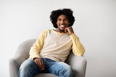 Yakışıklı genç siyah bir adam koltukta rahatça oturur ve kameraya gülümser. Evde rahat bir anın tadını çıkarıyor, rahat bir ortamda neşe ve sıcaklık yayıyor..