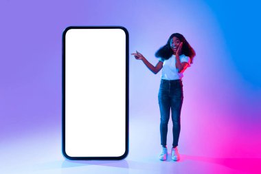 Kıvırcık saçlı genç bir kadın büyük boş bir akıllı telefonu işaret ederken sevinç ifade eder. Arka planda parlak mavi ve pembe renkler var, canlı bir atmosfer yaratıyor..