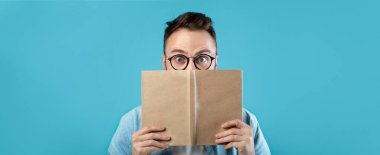 Gözlüklü bir adam boş bir kitabı yüzünün önünde tutuyor. Şaşırmış ve şaşırmış görünüyor. Arka plan canlı bir mavi, sahnenin neşeli hissini ekliyor..