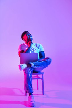 Renkli neon bir ortamda, düşünceli genç siyah bir adam bir sandalyeye oturur, dizüstü bilgisayarını tutar ve yukarıya bakar. Sanal bir toplantı ya da internet işi sırasında derin düşüncelere dalmış gibi görünüyor..