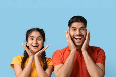 İki genç insan mutlu bir anı kutluyor. Elleri yüzlerinde neşeli ifadeler sergiliyorlar. Parlak mavi arka plan neşeli atmosfere katkı yapıyor..