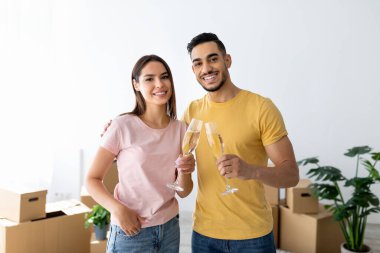 Mutlu bir çift, ellerinde şampanya kadehleriyle parlak bir odada yan yana durur. Neşeli bir şekilde gülümserler, yeni hayatlarının başlangıcını kutlarlar paketlenmemiş kutularla çevrili olarak..