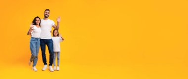 Neşeli bir aile birlikte güneşli bir anın tadını çıkarır. Baba, anne ve kız canlı sarı bir arka planda mutlu bir şekilde poz veriyorlar, hepsi günlük kıyafetler giyiyorlar, sıcak ve davetkar bir sahne yaratıyorlar..