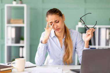 Bayan bir ofis çalışanı masasında oturur ve burun köprüsüne yorgun bir ifadeyle masaj yapar. Dizüstü bilgisayarı üzerinde uzun saatler çalıştıktan ve görme zorluğu çektikten sonra bitkin görünüyor..