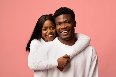 Neşeli siyah bir çift pembe bir stüdyoda birbirine sarılıyor. Kadın erkek arkadaşına arkadan sarılıyor, ikisi de beyaz kazaklar giyiyor ve mutlulukla gülümsüyor. Birlikte eğlenceli bir anı paylaşıyorlar..