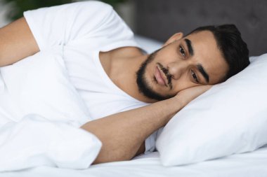 Genç bir Arap adam yatakta gözleri açık uzanıyor, dalgın ve üzgün görünüyor. Evde dinlenmeye çalışırken uykusuzluk çekiyor. Etrafı sakin bir yatak odası atmosferiyle çevrili..