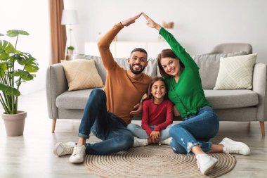 Ebeveynler, sıcak oturma odalarında halının üzerinde oturan neşeli kızlarına ellerini sürerek koruyucu bir çatı oluştururlar. Atmosfer sevgi ve sıcaklıkla dolu..